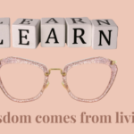 Wooden letter blocks spelling LEARN above stylish reading glasses with the phrase "Wisdom comes from living," symbolizing life experience, growth, and personal wisdom.